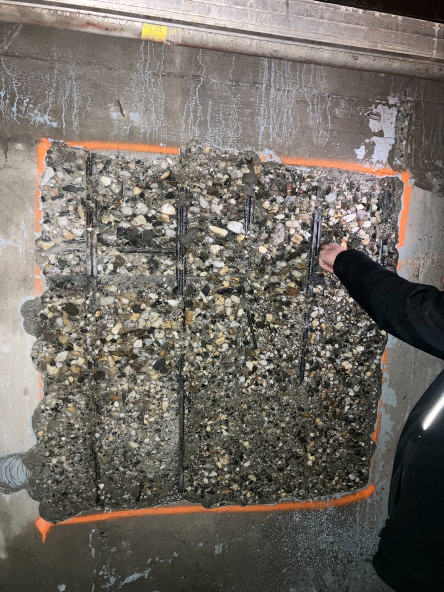 Betonová výplň s kamenivem a armaturou v otvoru ve zdi, pracovník drží ruku u okraje. Ukázka hydrodemolice betonů
