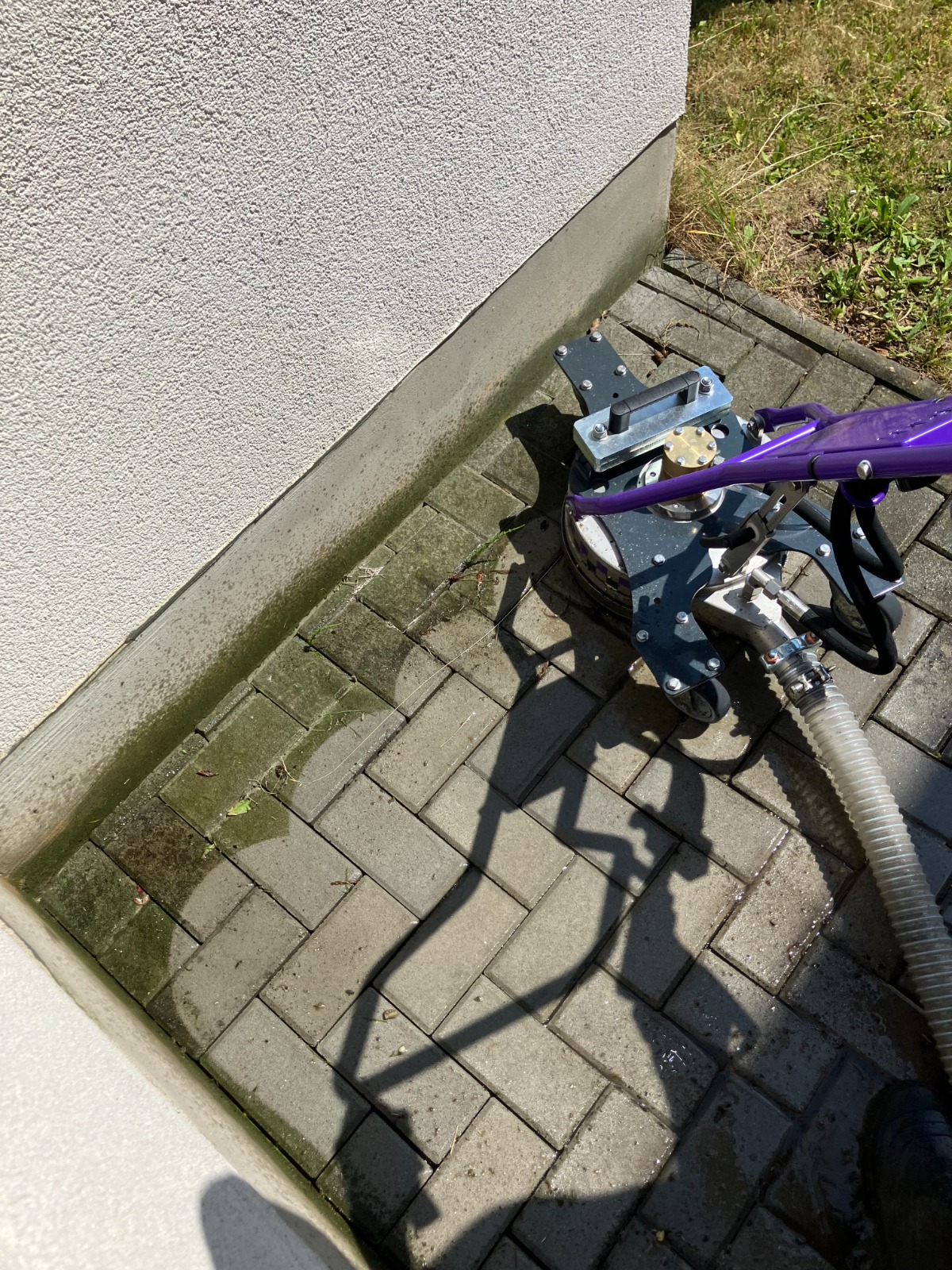 Fialový zahradní postřikovač s kovovým mechanismem na dlažbě u bílé zdi, ve slunečním světle.

Vysokotlaké čištění dlažby scatterem. Falch 